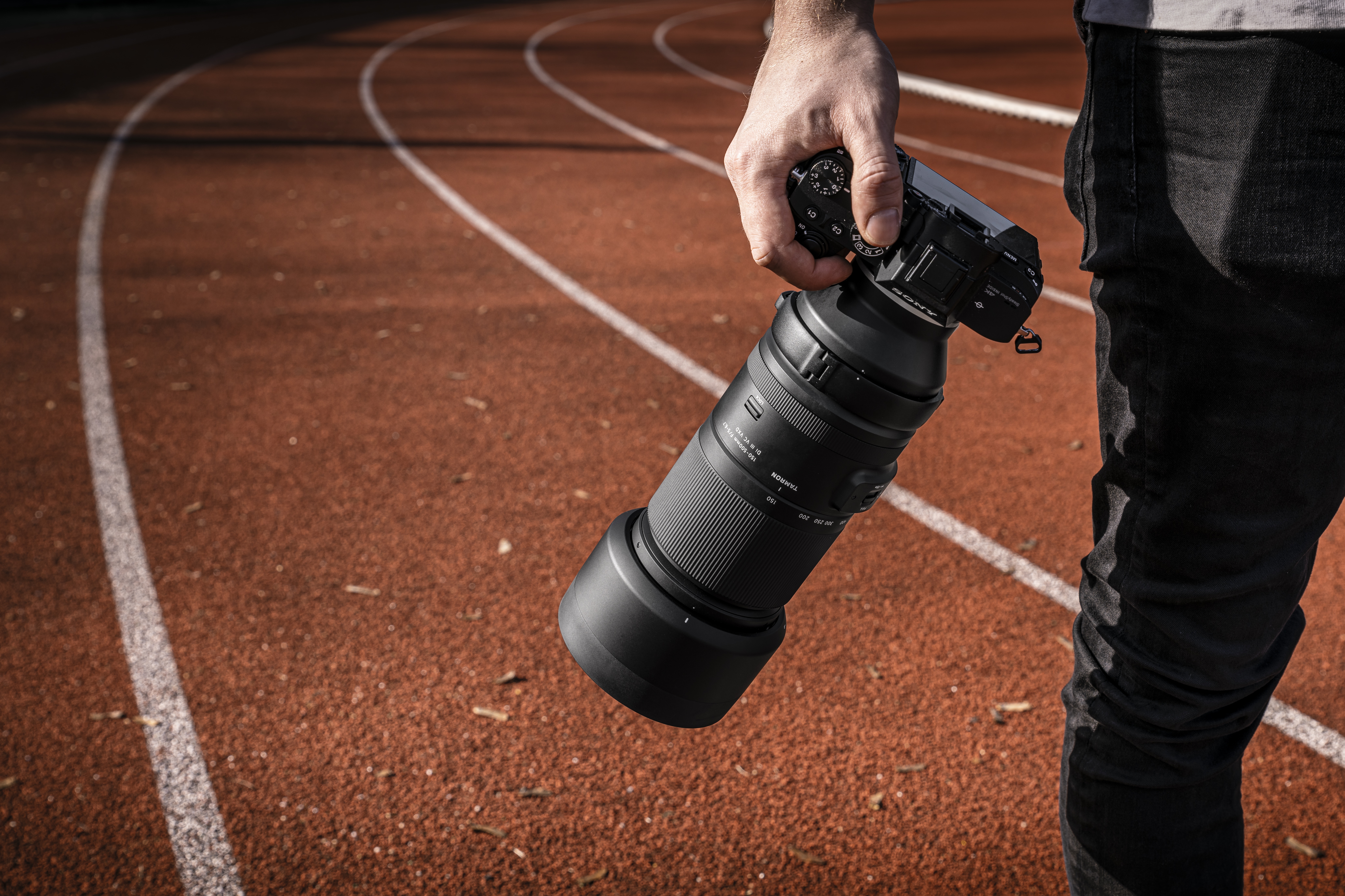Objektiv Tamron na fotoapar&aacute;tu Sony v ruce fotografa na běžeck&eacute; dr&aacute;ze